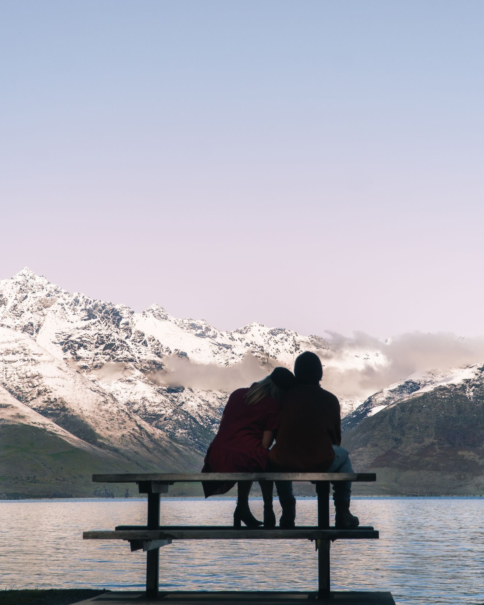 Romantic couple sitting on a bench admiring a lake and mountains